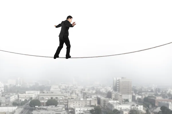 Businessman balancing and walking on the rope with urban scene — Stock fotografie