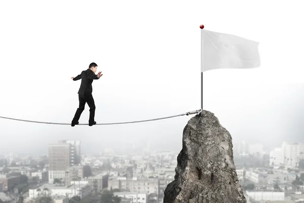 Businessman walking on rope toward white flag with cityscape — Zdjęcie stockowe