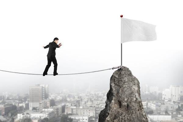Businessman walking on rope toward white flag with cityscape