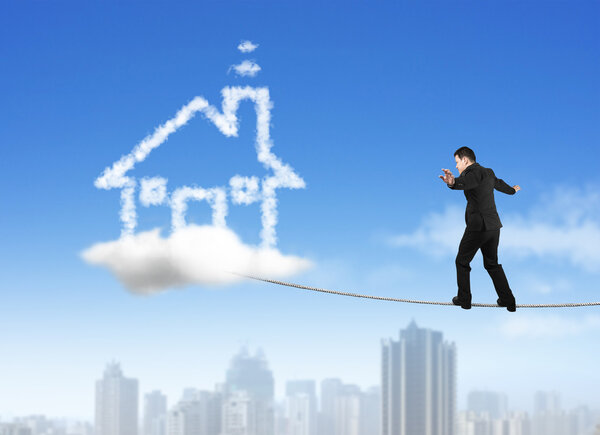 Businessman walking on rope toward house shape cloud with skyscr