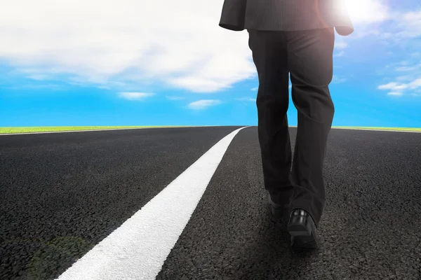 Homme d'affaires marchant sur la route asphaltée avec un ciel bleu ensoleillé — Photo