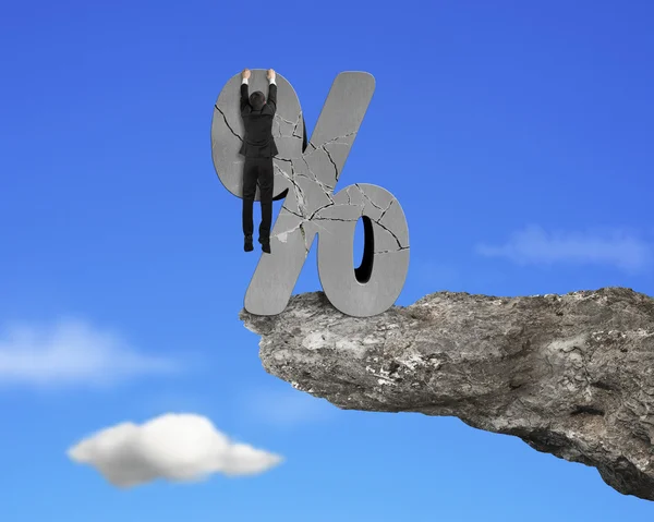 Businessman hanging on cracked percentage sign with cliff sky — Stock fotografie