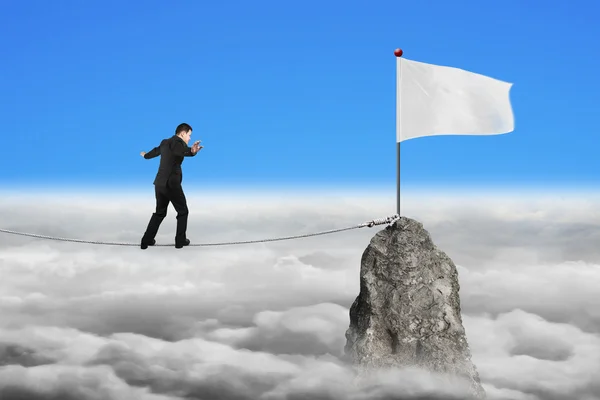 Empresario caminando en cuerda hacia bandera blanca con paisaje nublado —  Fotos de Stock