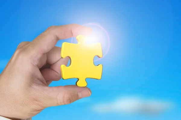 Hand holding gold jigsaw puzzle piece with blue sky sunlight — Stok fotoğraf