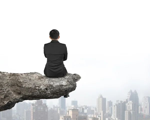 Rear view businessman sitting on cliff with urban skyscrapers — Stockfoto