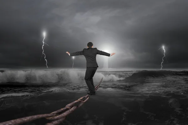 Businessman balancing on old iron chain with dark stormy ocean — Stockfoto
