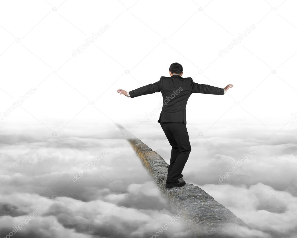 Businessman balancing on concrete ridge with gray cloudy sky