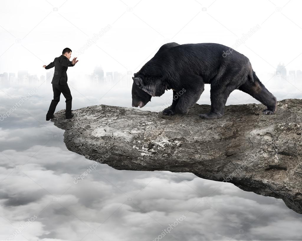 Businessman against black bear balancing on cliff with cloudy sk
