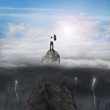 Businessman cheering on mountain peak with sunny sky cloudy ligh