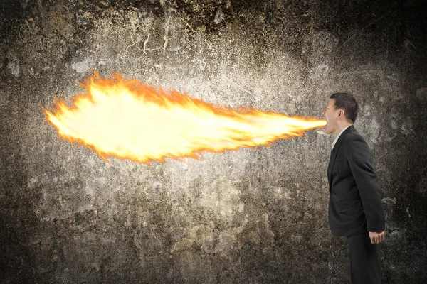 Angry businessman spitting fire from mouth illuminated dark wall — Stockfoto