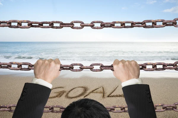 Businessman climbing on iron chains with goal word sand beach — Zdjęcie stockowe