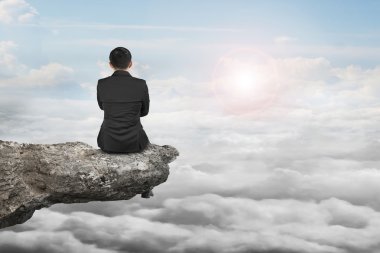 Rear view businessman sitting on cliff with natural daylight clo