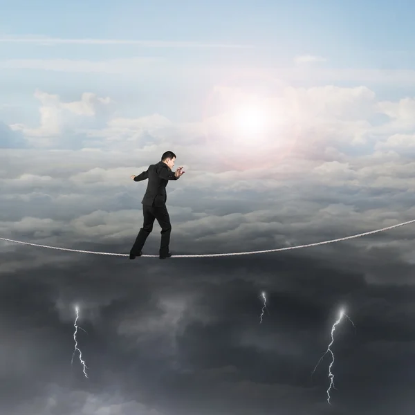 Caminante hombre de negocios equilibrio en la cuerda con el cielo del sol relámpago nublado — Foto de Stock