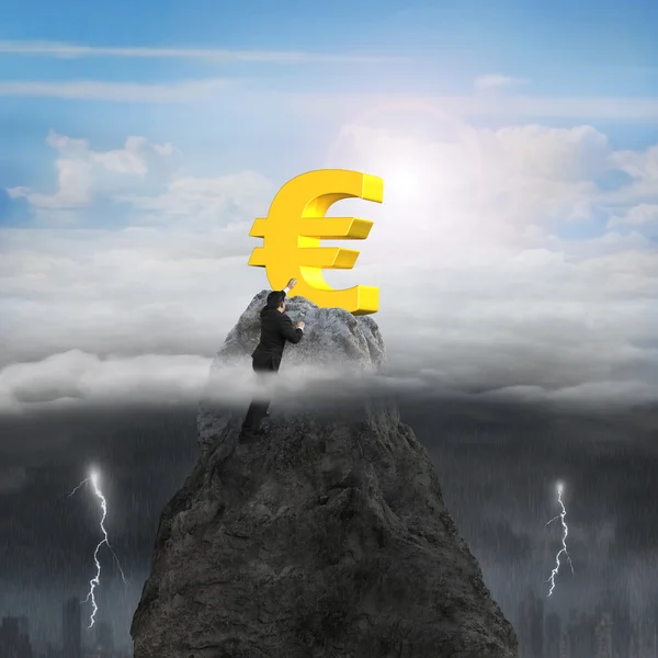 Empresario mano queriendo euro símbolo en pico con tormenta soleada — Foto de Stock