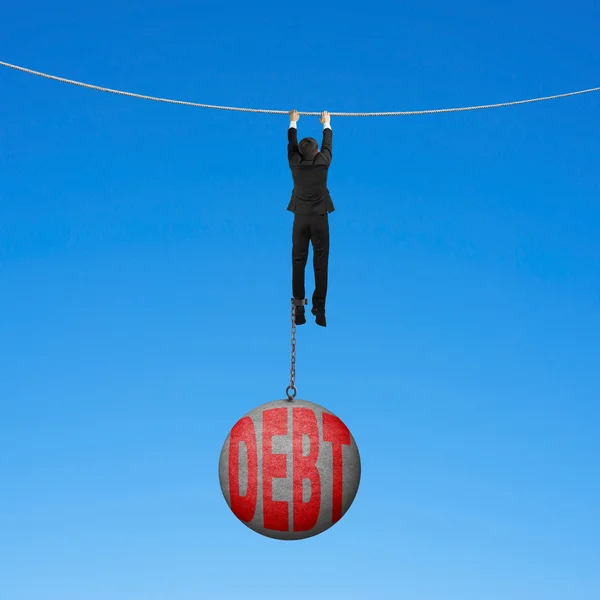 Businessman shackled by debt ball hanging on rope blue backgroun — Stock Photo, Image