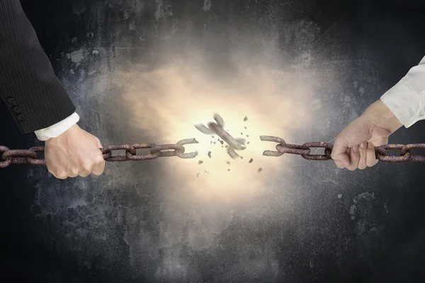 Businessman pulling rusty iron chains broken with dark concrete 