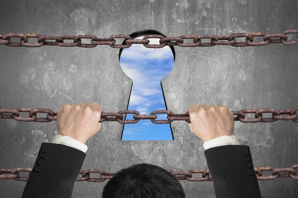 Businessman climbing on iron chain for keyhole with sky clouds — Stock fotografie