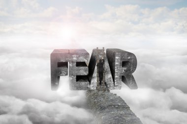 Businessman climbing ladder conquering fear word on ridge with s