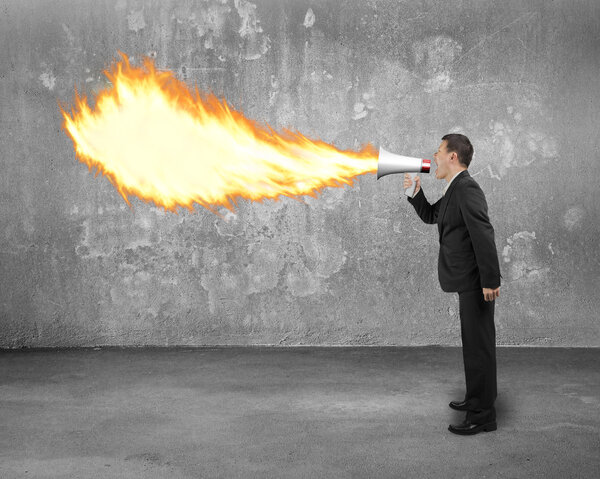Angry businessman screaming into megaphone spitting fire with co