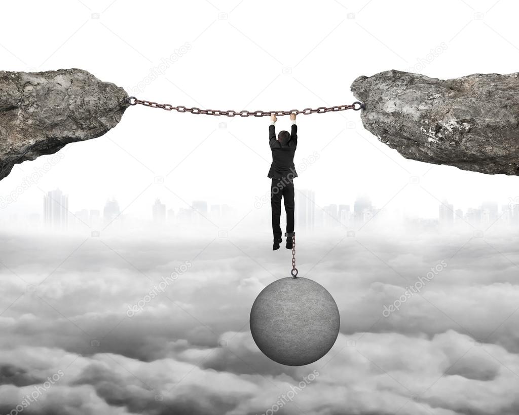 Businessman shackled by ball hanging on iron chains connected cl