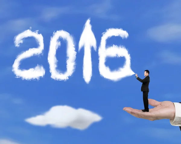 Mão segurando homem de negócios pulverizando 2016 seta para cima nuvens com céu — Fotografia de Stock