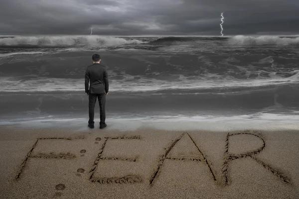 Rear view businessman standing facing fear word on sand beach — Stock Photo, Image