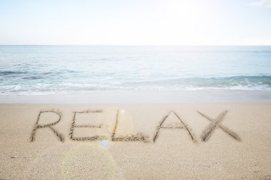 Relax word handwritten in sand on sunny beach