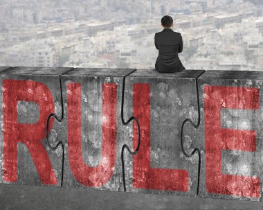 Business man sitting on concrete puzzles with red rule word