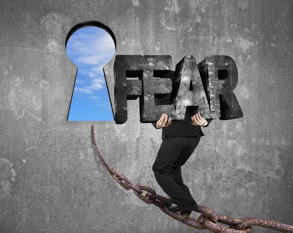 Man carrying fear word on chain toward keyhole with sky — Stockfoto