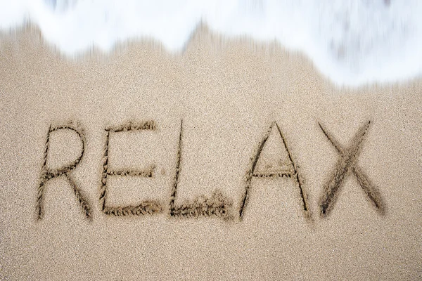 Расслабьте слово, написанное от руки на пляже — стоковое фото