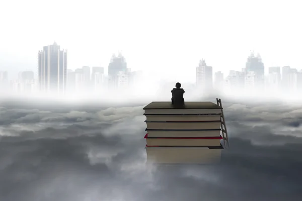 Pondering man sitting on stack of books with cityscape cloudscap — 스톡 사진