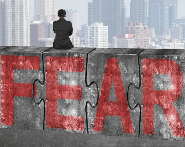 Businessman sitting on huge concrete puzzles with red fear word — Φωτογραφία Αρχείου