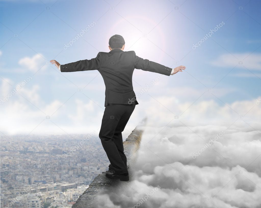 Businessman balancing on concrete ridge with sky sunlight clouds