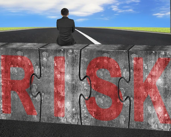 Businessman sitting on huge concrete puzzles with red risk word — Stock fotografie