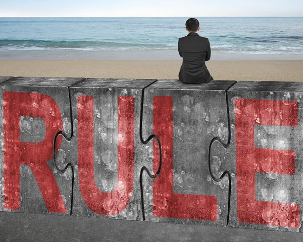 Businessman sitting on huge concrete puzzles with red rule word