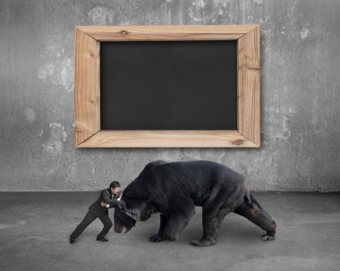 Businessman fighting against black bear with blank blackboard