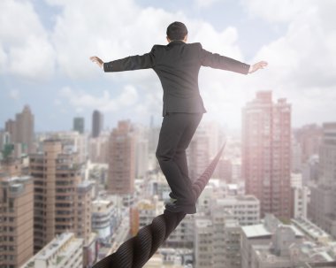 Businessman balancing on a wire with sky clouds cityscape