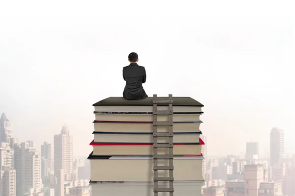 Uomo d'affari seduto su pila di libri con scala in legno — Foto Stock