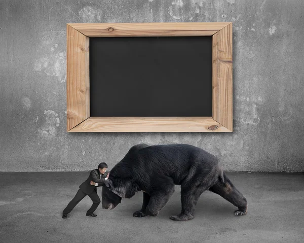 Businessman fighting against black bear with blank blackboard — 图库照片