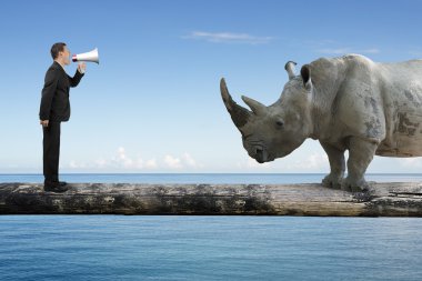 Businessman using speaker yelling at rhinoceros on single wooden