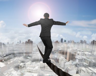 Businessman balancing on a wire with sun mist cityscape clipart