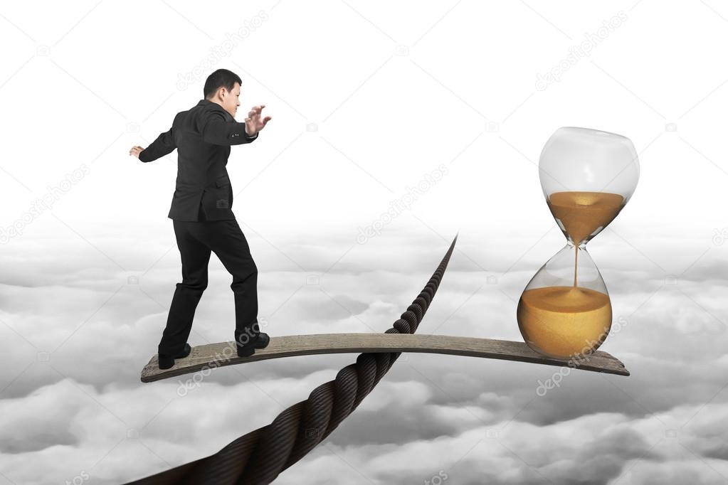 Businessman and hourglass on wood board balancing on wire