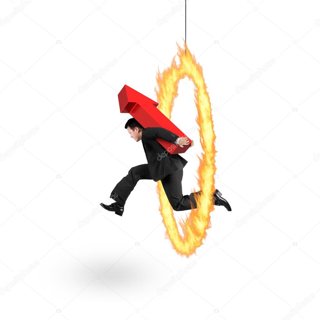 Businessman carrying red arrow up sign jumping through fire hoop