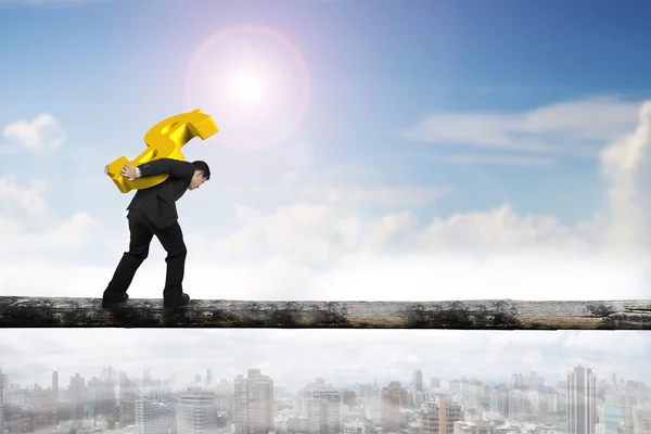 Businessman carrying golden dollar sign balancing on tree trunk — Stock Photo, Image