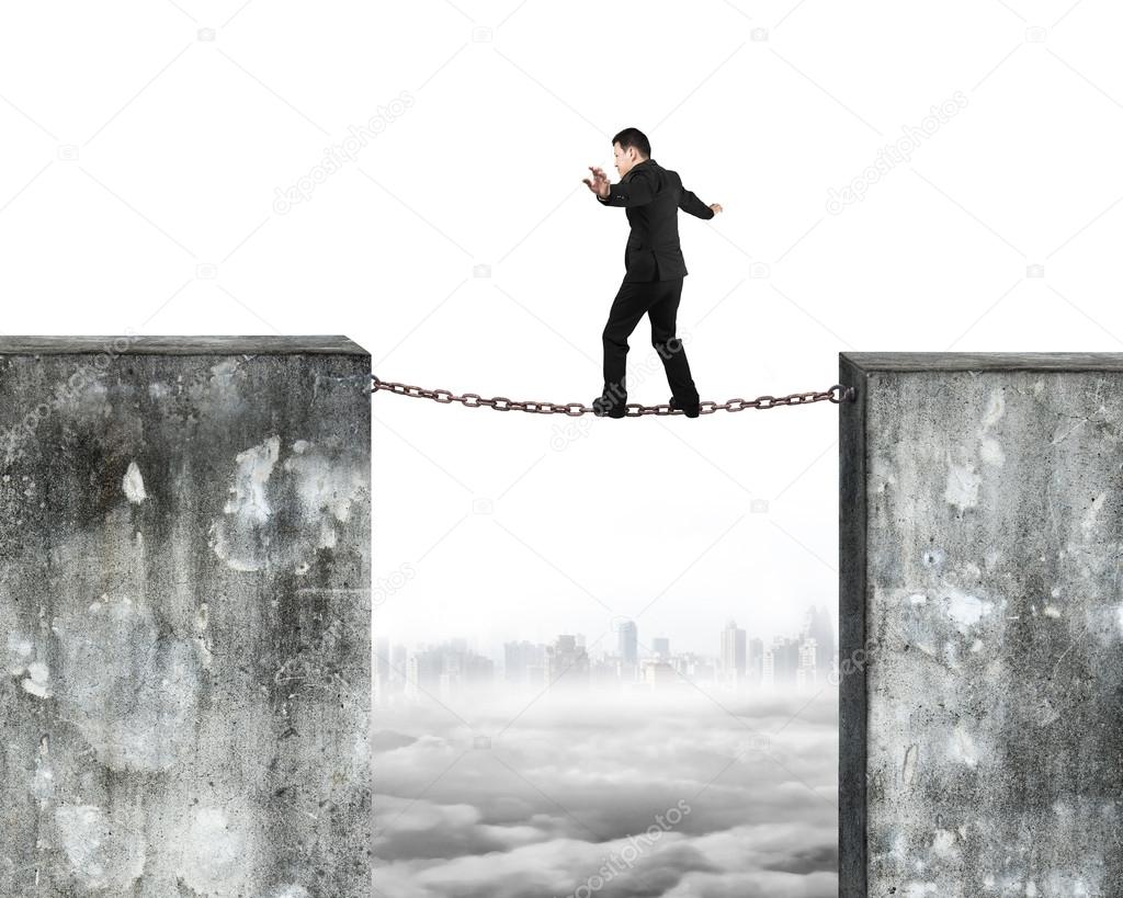 Businessman balancing rusty chain connected concrete walls