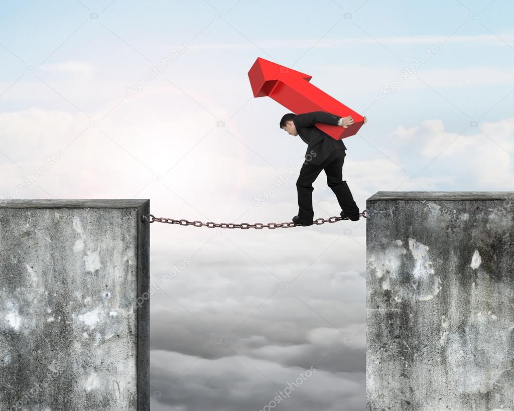 Businessman carrying red arrow sign balancing on rusty chain