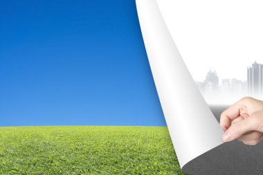 Woman hand turning gray cityscape page revealing sky grass