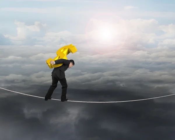 Businessman carrying golden dollar sign balancing on tightrope — Stock Photo, Image