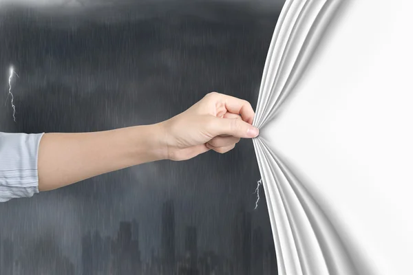 Vrouwelijke hand trekken lege witte gordijn die betrekking hebben op stormachtige stad — Stockfoto