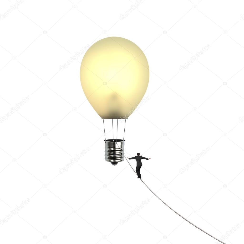 Businessman walking tightrope toward lightbulb shape hot air bal